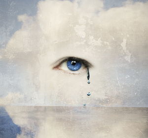 A tear drop falls from an eye just seen through the clouds