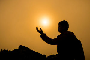Silhouette of man kneeling and praying over beautiful sunrise on mountain background, seeking to reconnect with someone who has passed.